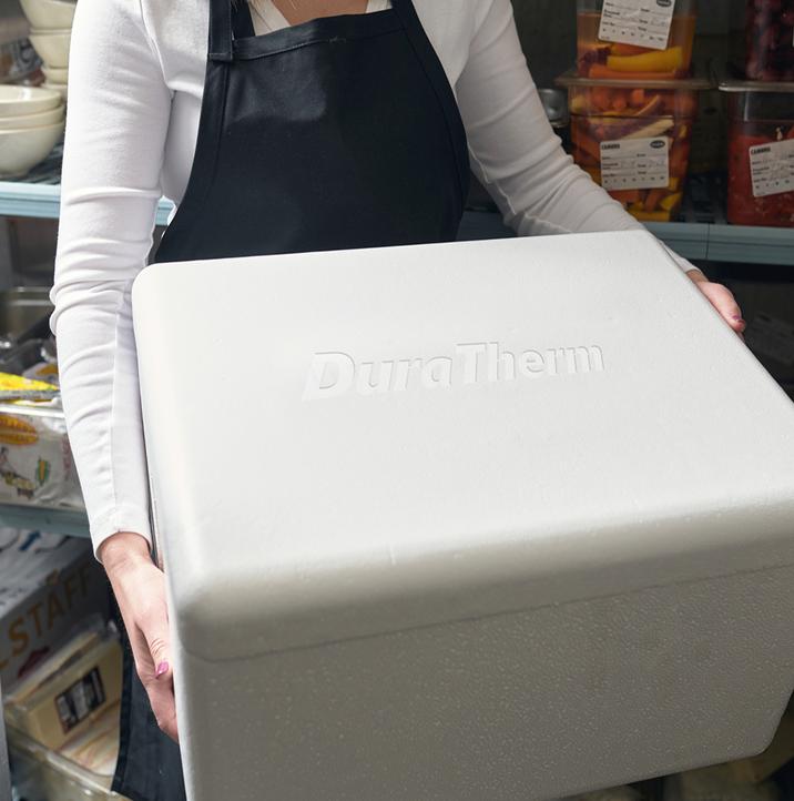 Worker holding an insulated foam packaging container in a refrigerated storage room.